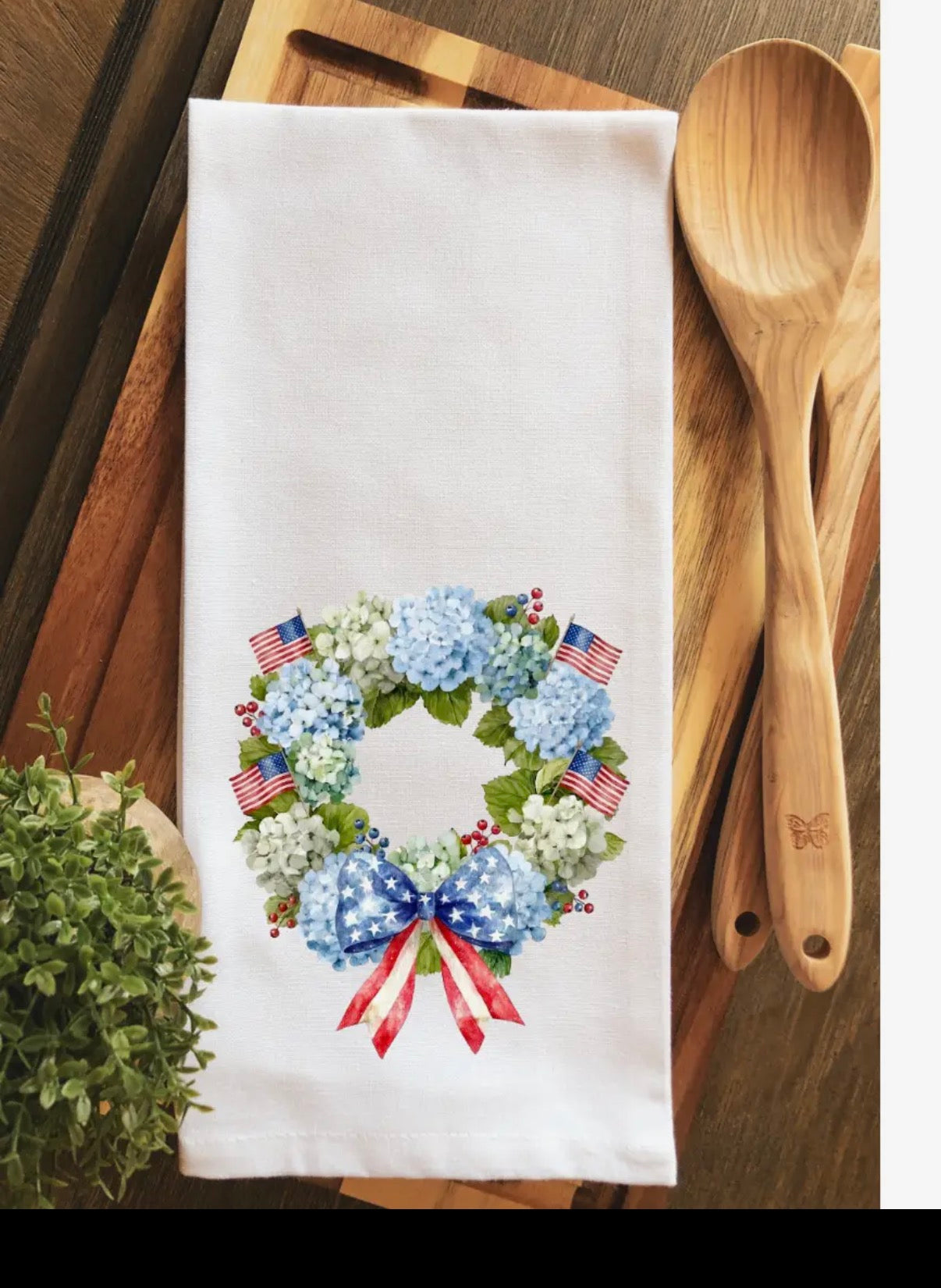 Decorative towel with floral and American flag design on a wooden cutting board with utensils.