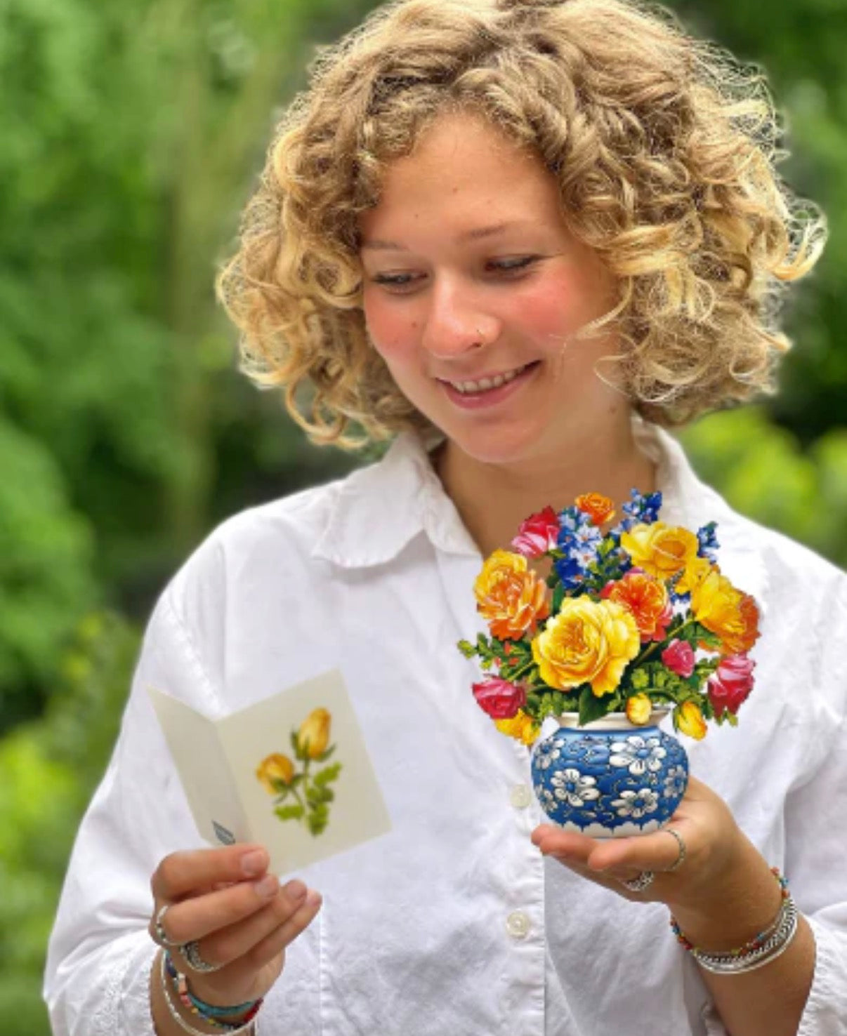 Woman holding a vase of flowers and a card with floral design outdoors