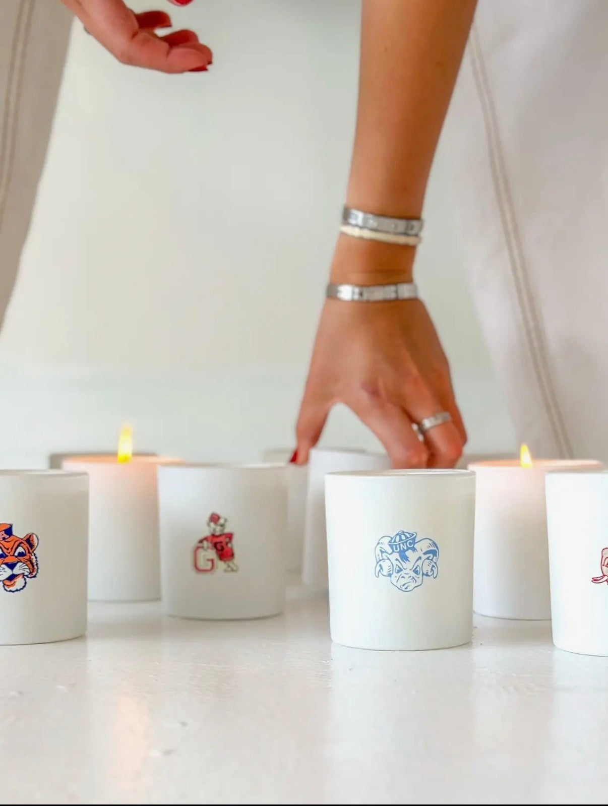 Candles with decorative labels on a white surface, with a hand reaching to light one.