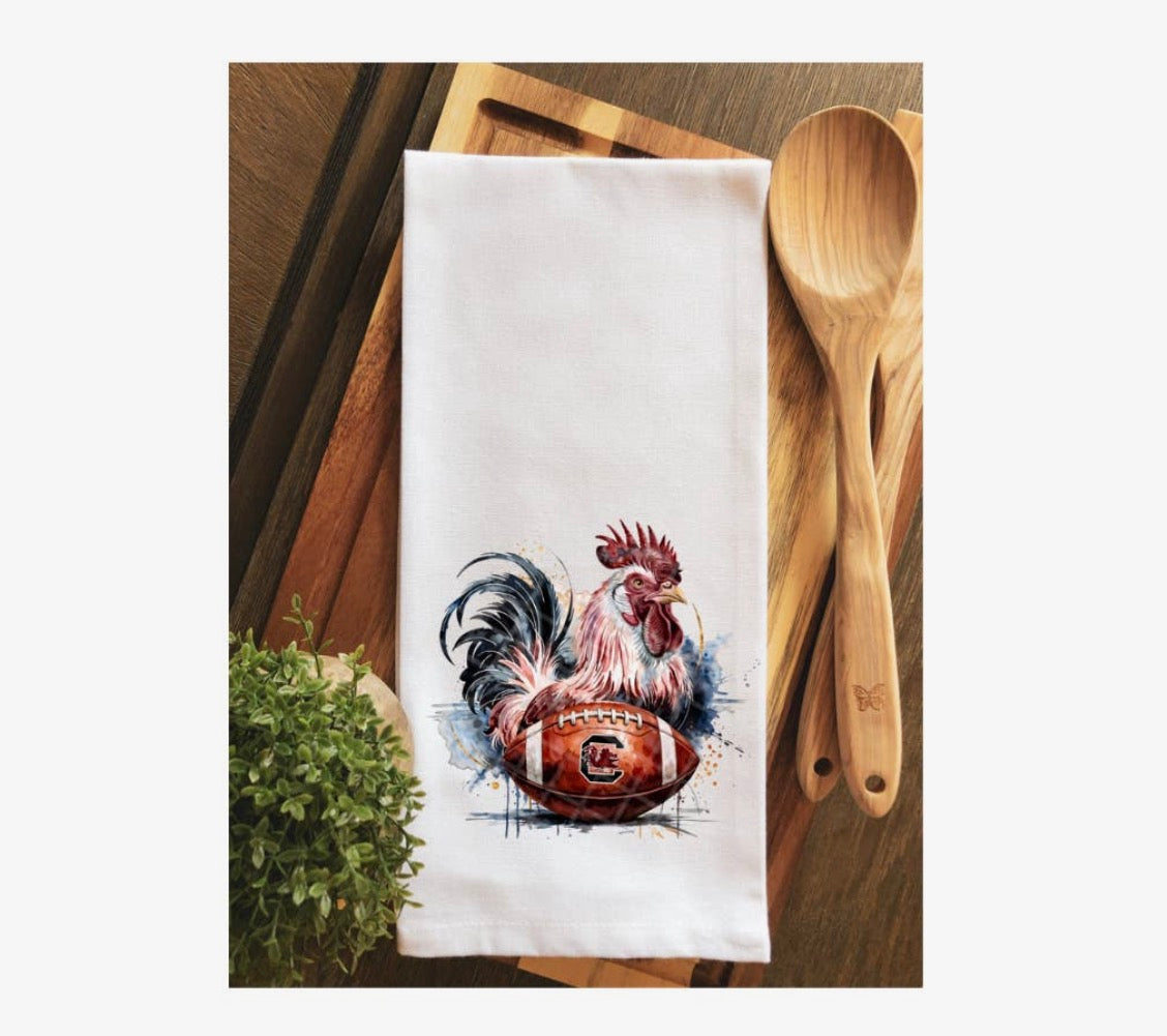 White towel with rooster and football design on a wooden surface with wooden spoons.