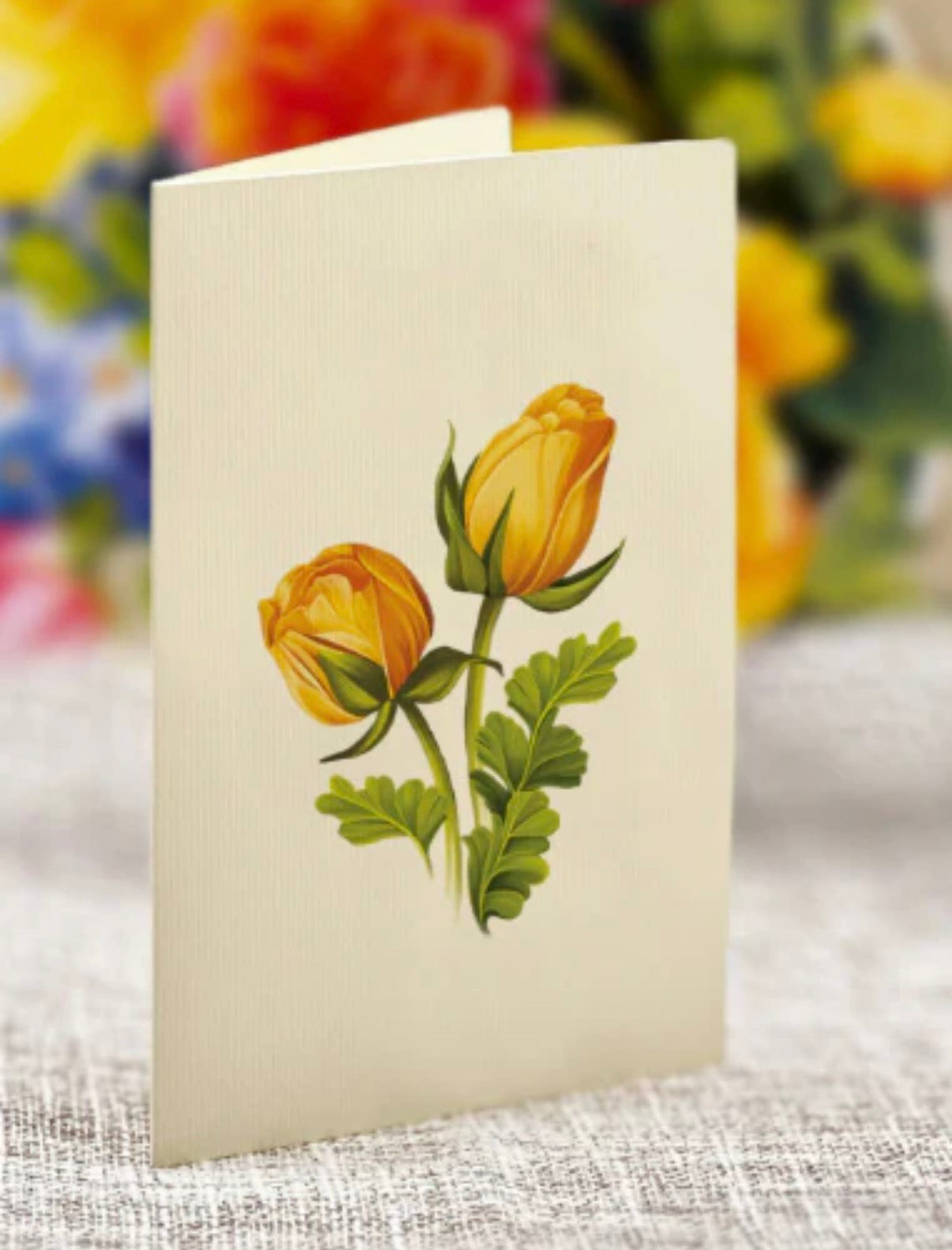 Card with yellow rose illustration on a textured surface with blurred floral background