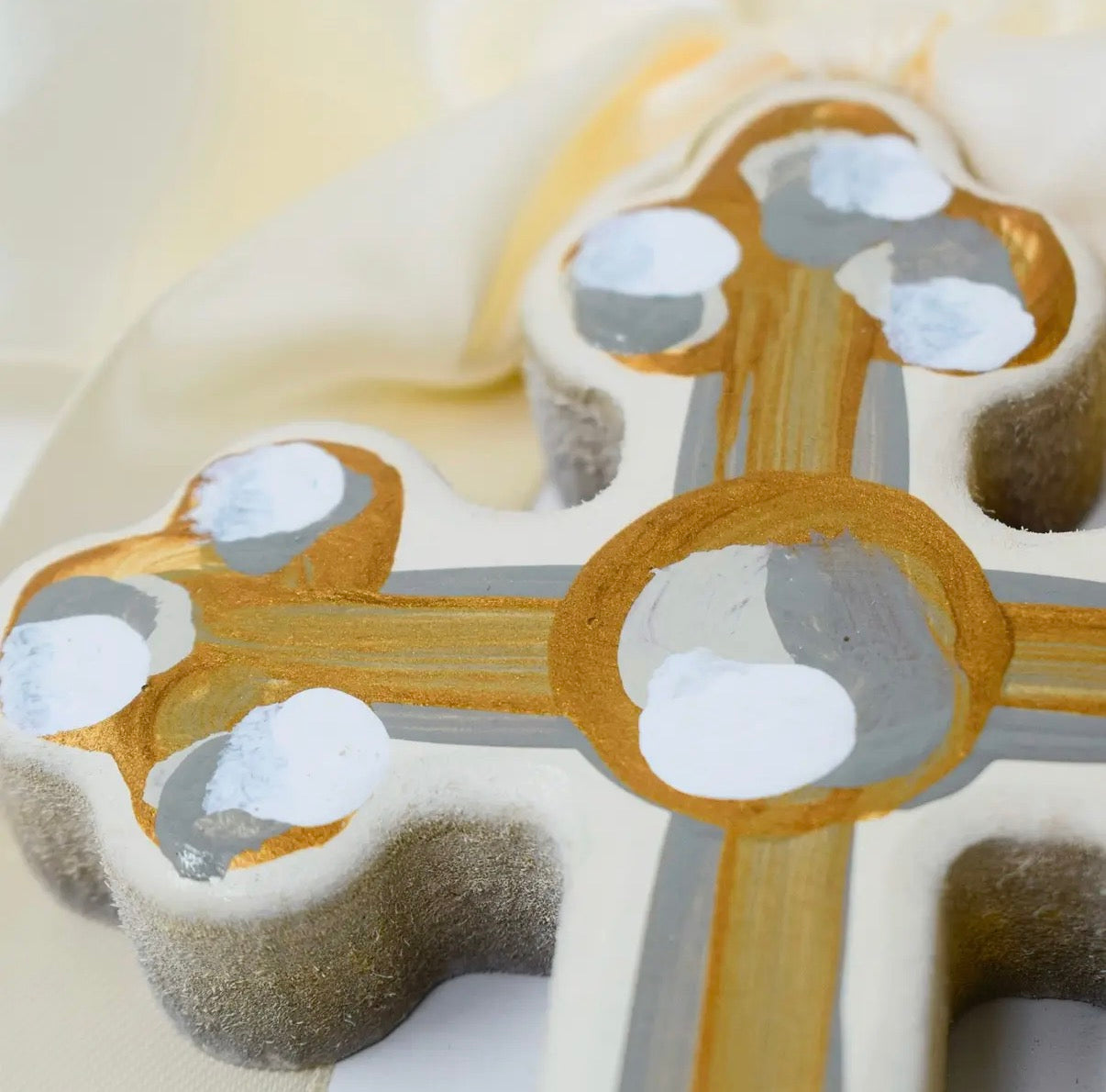 Close-up of a cross-shaped object with gold and silver elements on a light background