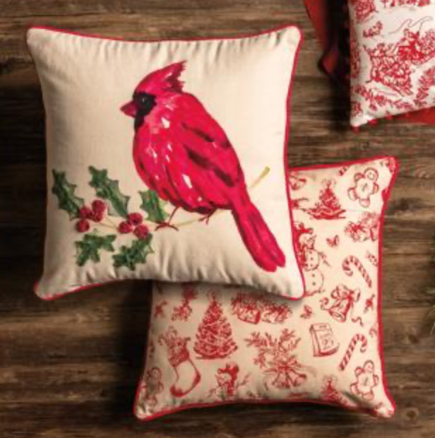 Decorative pillows with a cardinal design and Christmas-themed patterns on a wooden surface.