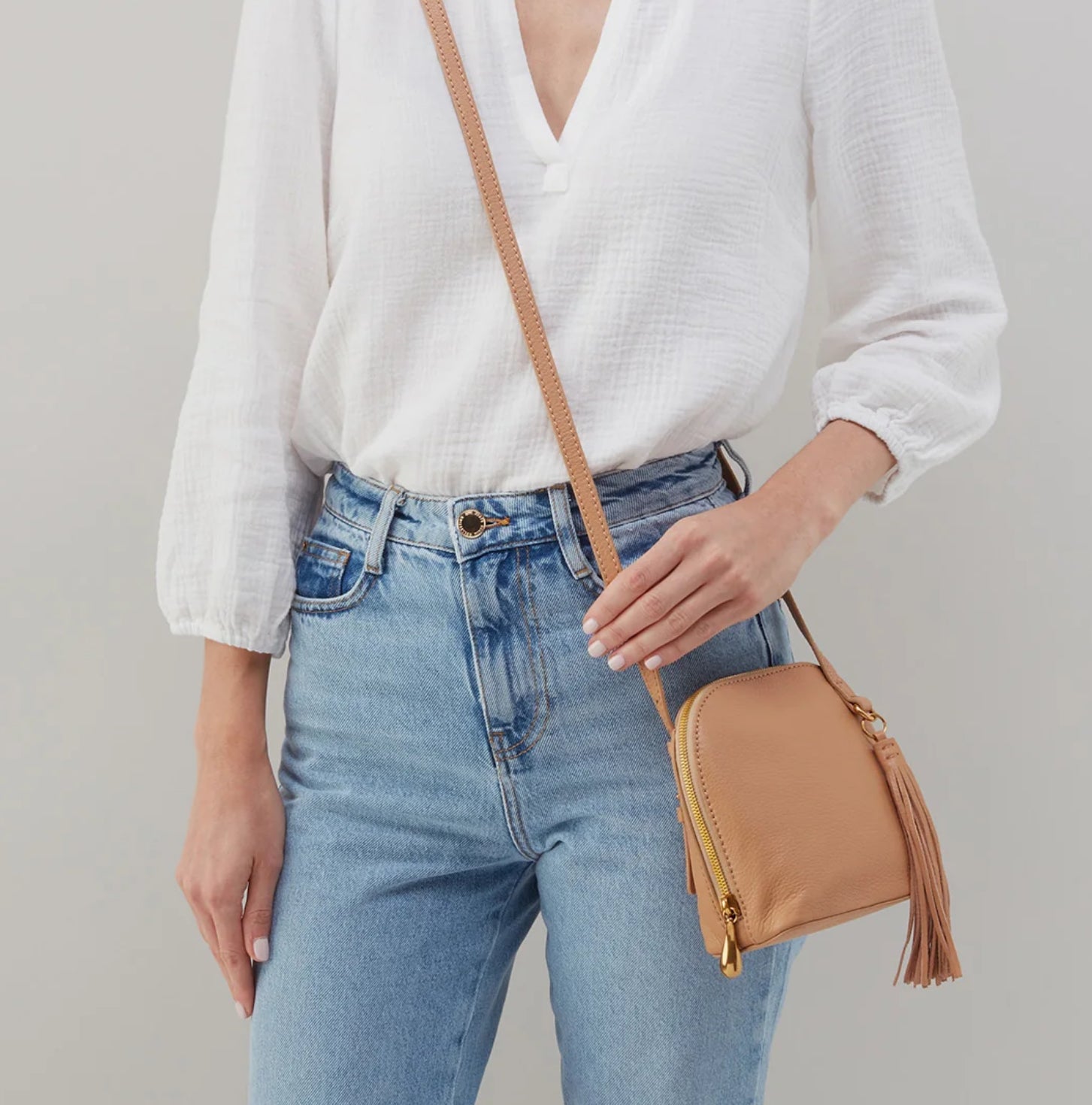 Accessories - Purse - Nash Crossbody - Sandstorm- brown purse being worn by a lady with a white top and jeans on a white background 