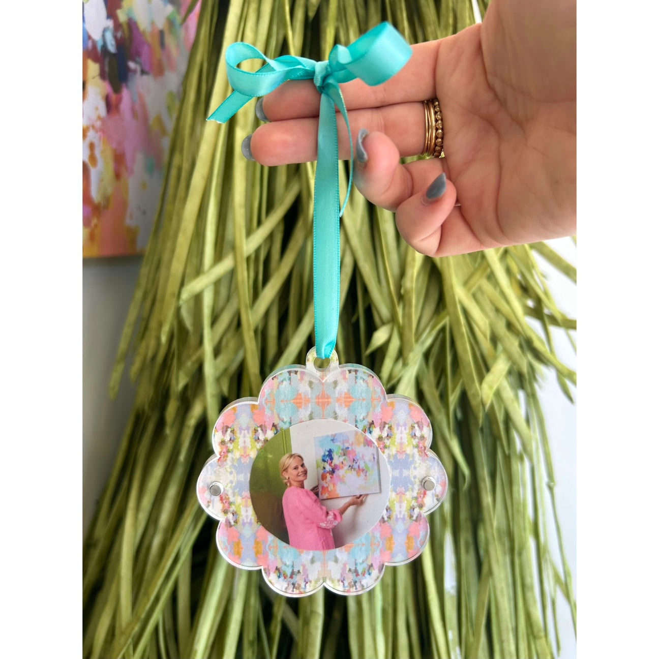 Decorative ornament with a photo of a woman in a pink dress, held by a hand with a teal ribbon.