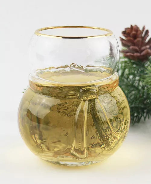 Glass jar with gold rim filled with a yellow liquid, possibly tea, on a white background.