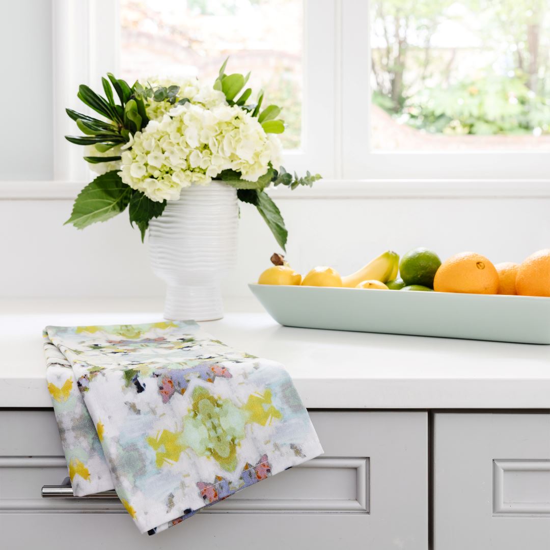Lady Bird Tea Towel Floral-patterned towel on a kitchen counter with a vase of flowers and fruit bowl in the background.
