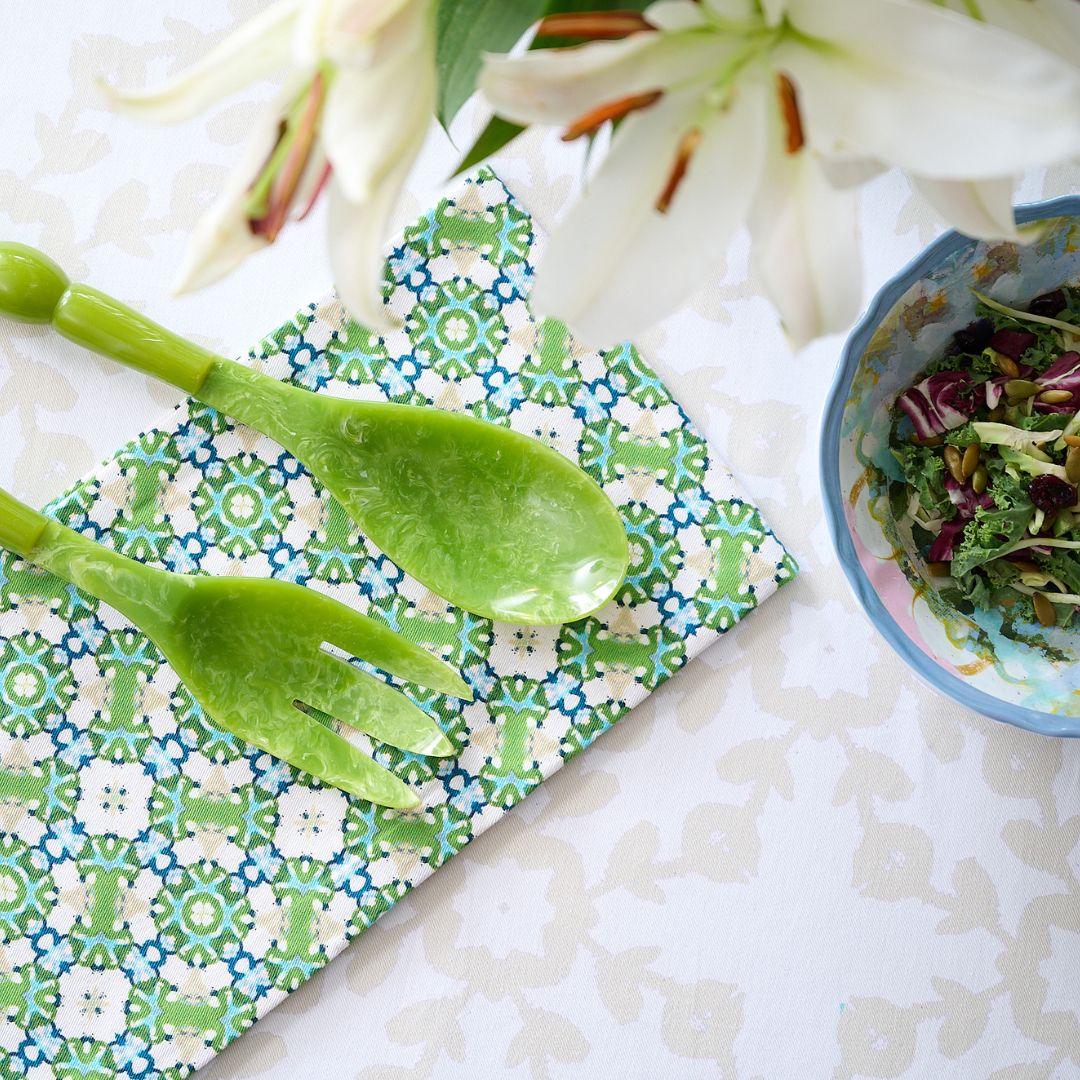 Green salad servers on a Serendipity Tea Towel with a bowl of salad and white flowers in the background.