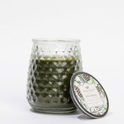 Green candle in a textured glass jar with a decorative lid on a white background