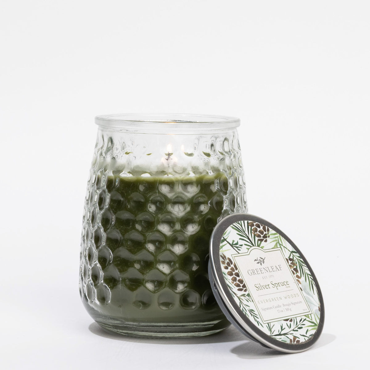 Green candle in a textured glass jar with a decorative lid on a white background