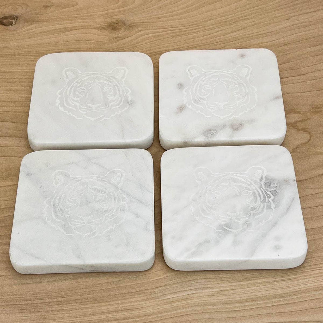 Four square marble coasters with a tiger face design by The Royal Standard on a wooden surface
