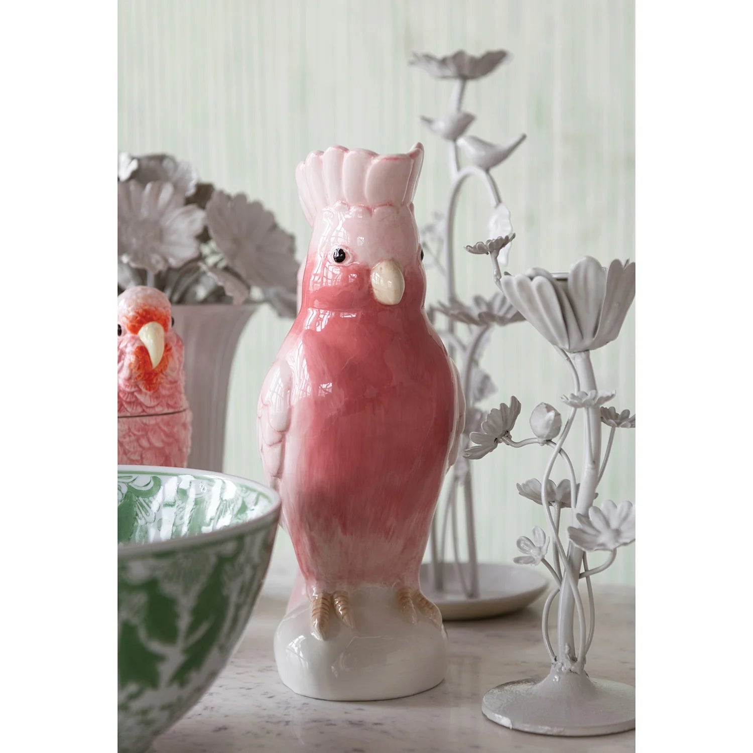 Pitcher - Ceramic - Cockatoo - 11 3/4 “ H- picture is a straight view of the pink ceramic cockatoo sitting on a table with other products 