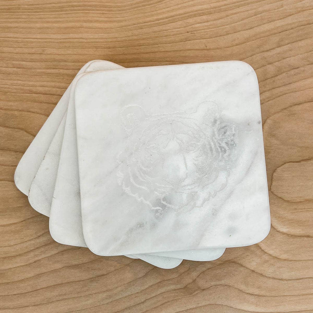 Four stacked square marble coasters with a tiger face design by The Royal Standard on a wooden surface