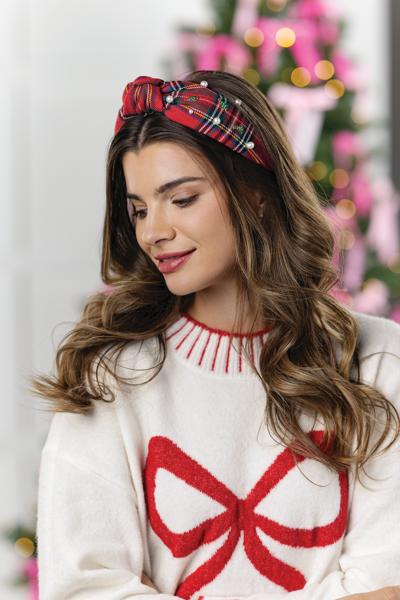Woman wearing a white sweater with a red bow and a plaid headband in a festive setting.