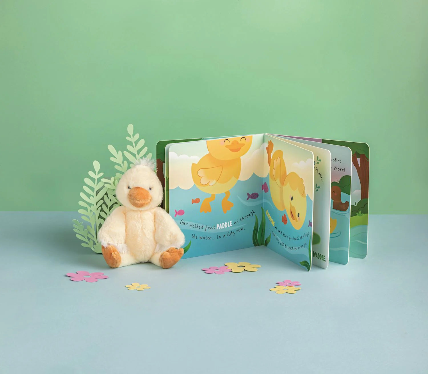 Children's book with duck illustrations and a plush duck toy on a light blue surface.