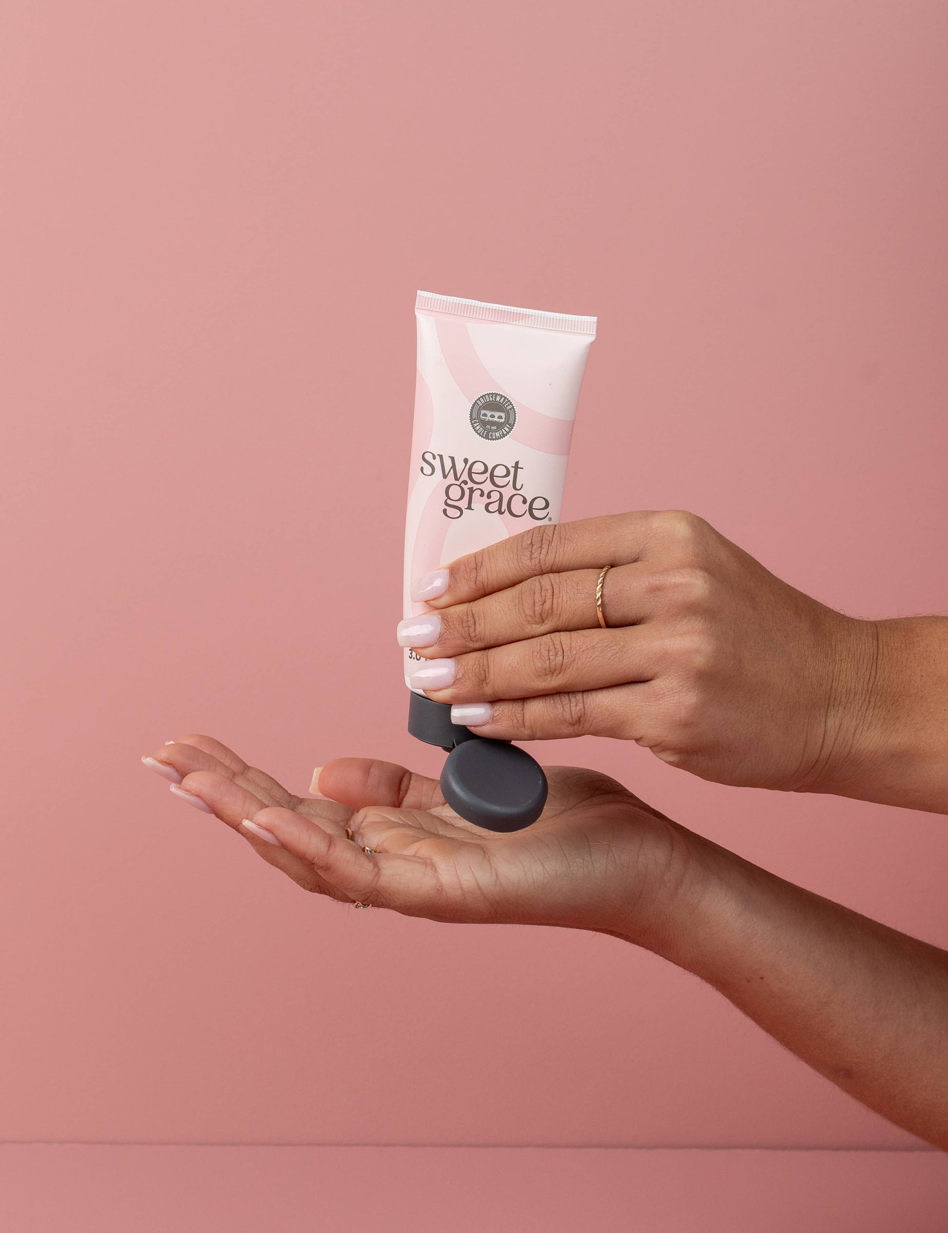 Woman applying Sweet Grace Hand Cream Pink Tube on a pink background
