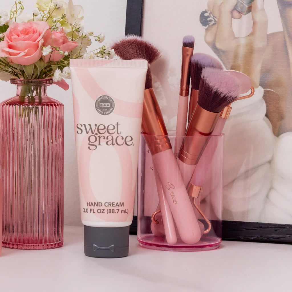 Sweet Grace Hand Cream Pink Tube on a dresser with flowers and makeup brushes in a pink cup