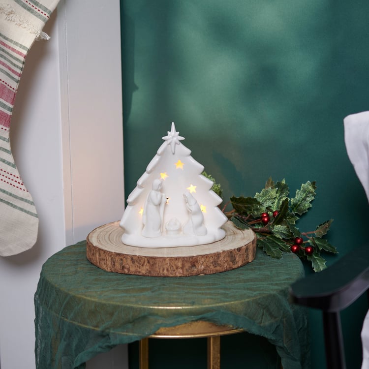 Decorative white ceramic Christmas tree with lights on a wooden base against a green wall.