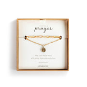Gold bracelet with a heart charm on a 'Wrapped in Prayer' card by Demiaco.