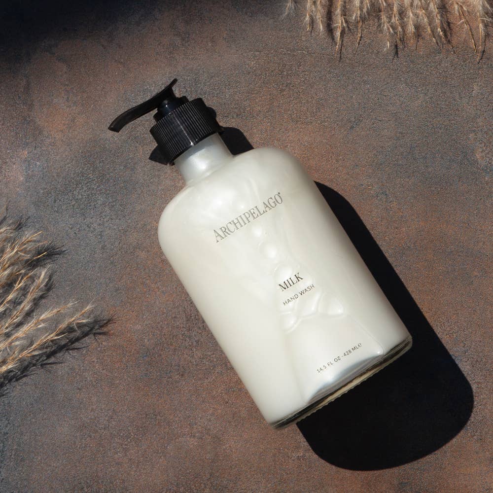 Archipelago Milk Hand Soap in a glass pump bottle on a dark brown table 
