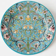 A decorative tin plate with a floral Art Deco design featuring a turquoise background and multicolored flowers and patterns.