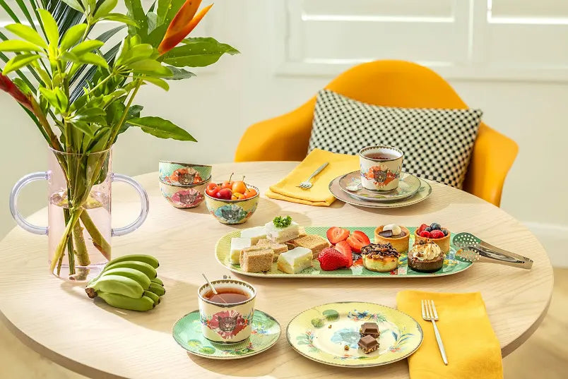 Round table with tea set, snacks, and fruit on a light-colored surface.