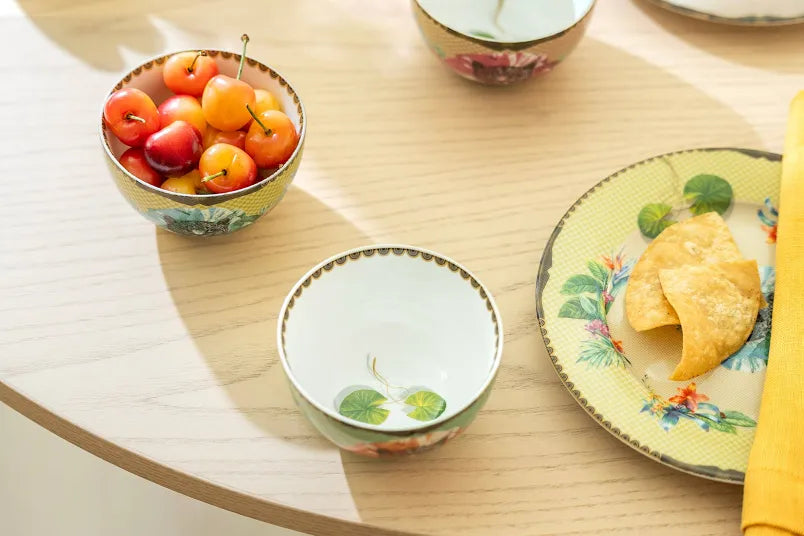 Decorative ceramic bowls and plate with fruit and floral patterns on a wooden table.