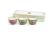 Three decorative ceramic cups with floral patterns in a wooden box on a white background