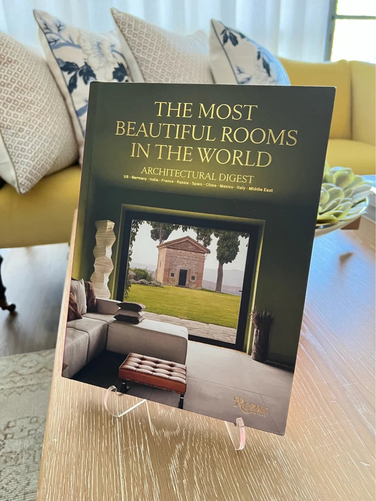 Book titled 'The Most Beautiful Rooms in the World' by Architectural Digest on a table with a living room background.