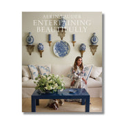 Book cover of 'Aerin Lauder Entertaining Beautifully' with a woman in a living room setting.
