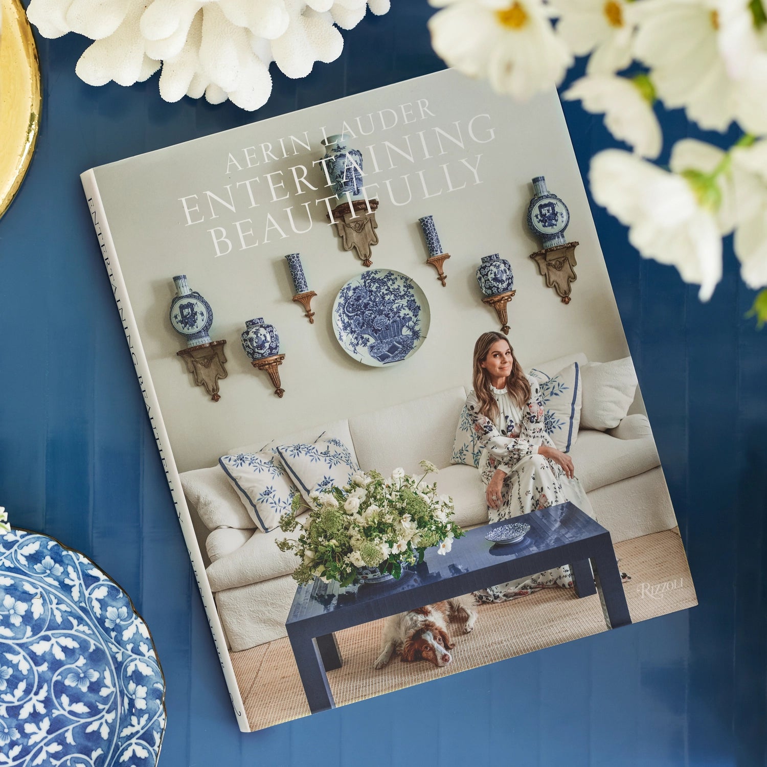 Book titled 'Entertaining Beautifully' with a woman sitting on a couch in a decorated room, surrounded by decorative items and flowers.