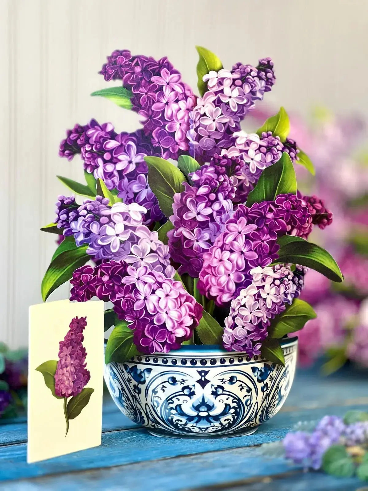 Bouquet of purple and white flowers in a decorative blue and white bowl on a wooden surface.
