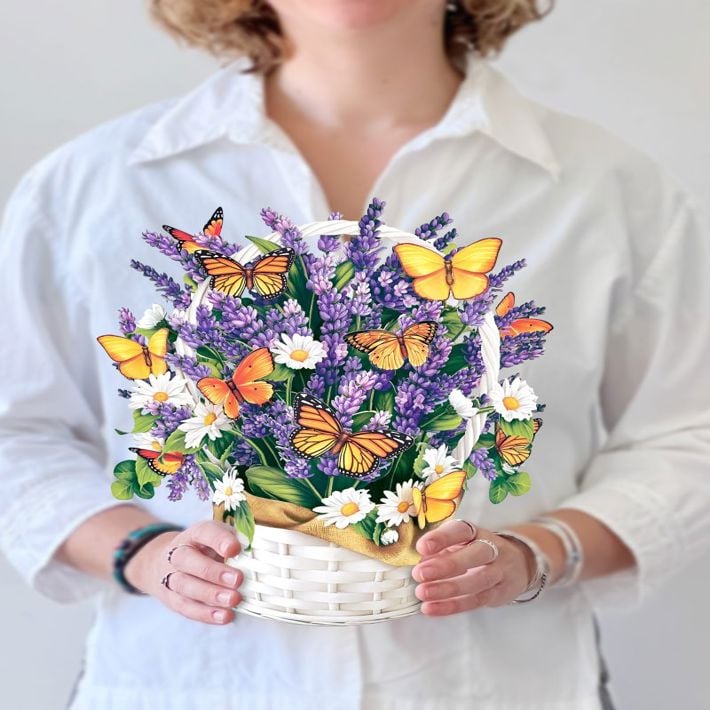 Person holding a basket of flowers with butterflies against a plain background
