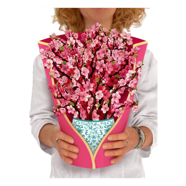 Person holding a large bouquet of pink flowers in a decorative pink and gold paper wrap.