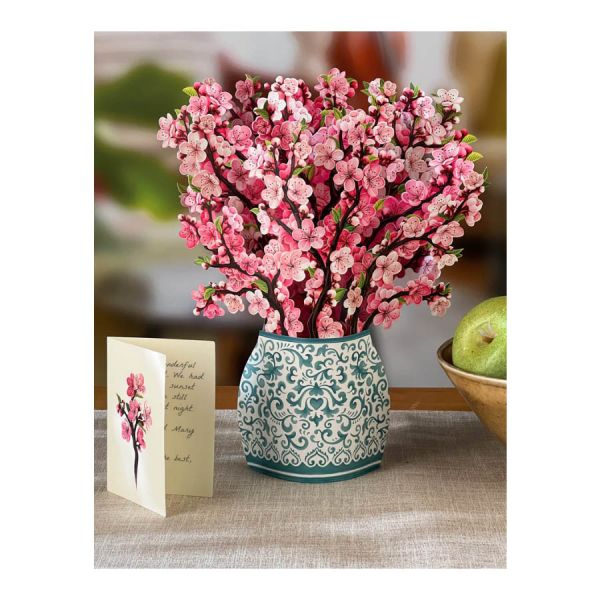Bouquet of pink flowers in a decorative vase on a table with a card beside it.
