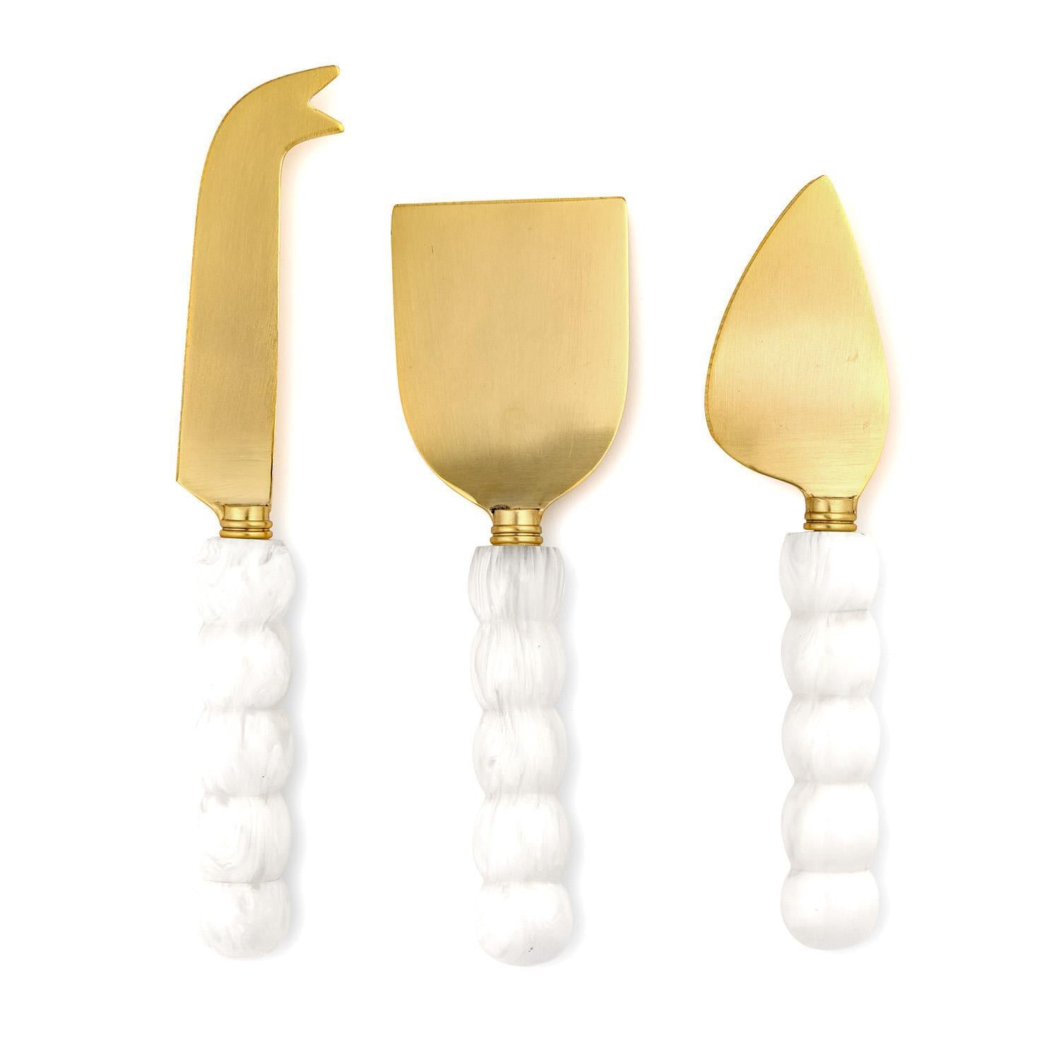 Set of three gold cheese knives with white chunky ball handles on a white background
