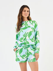 Woman wearing Mary Square In The Shade Pajamas, Nature inspired floral print shorts with long sleeve top. green, turquoise and white leaf-patterned on a white background