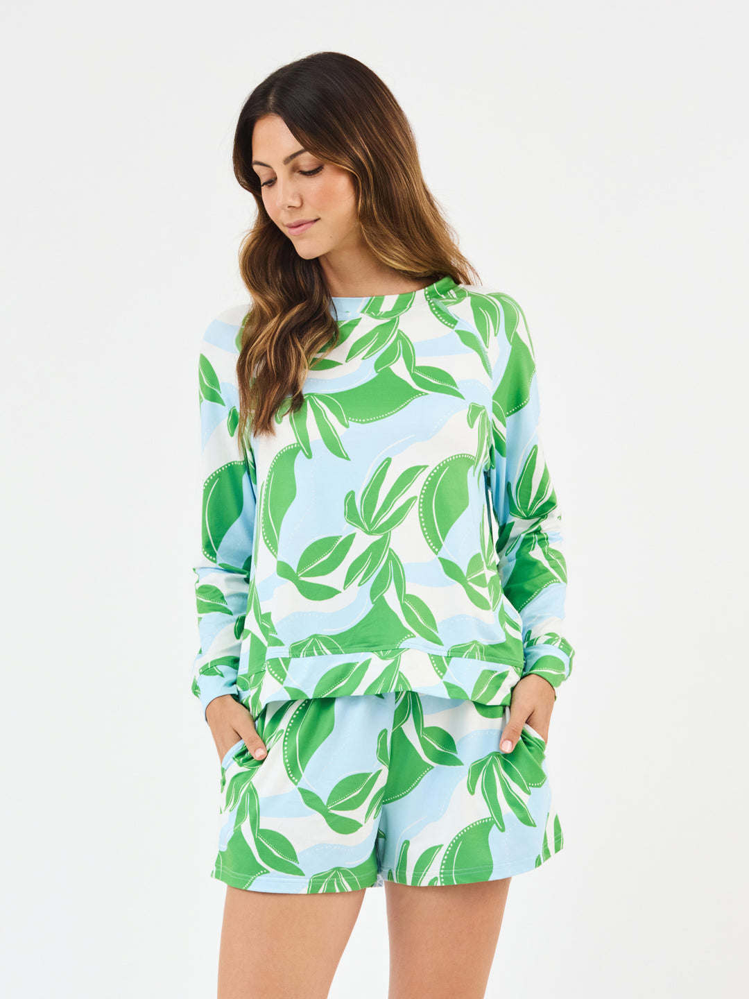 Woman wearing Mary Square In The Shade Pajamas, shorts with long sleeve top. green, turquoise and white leaf-patterned on a white background
