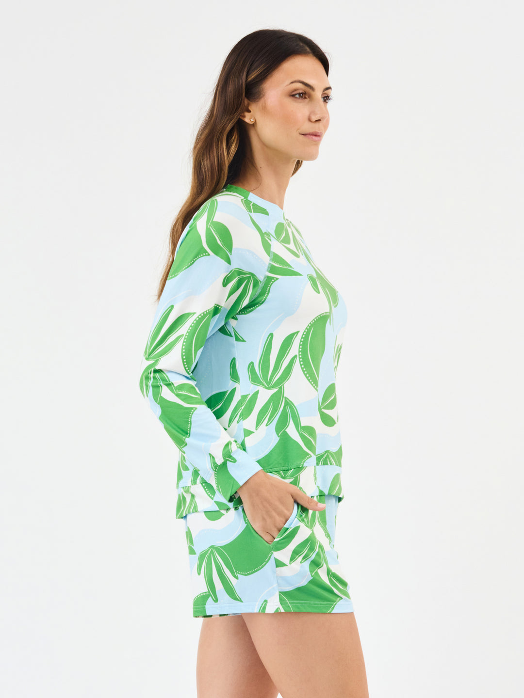 Woman wearing Mary Square In The Shade Pajamas. green, turquoise and white leaf-patterned with shorts and long sleeve top on a white background