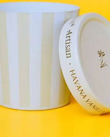 Candle container with lid propped on a yellow background 