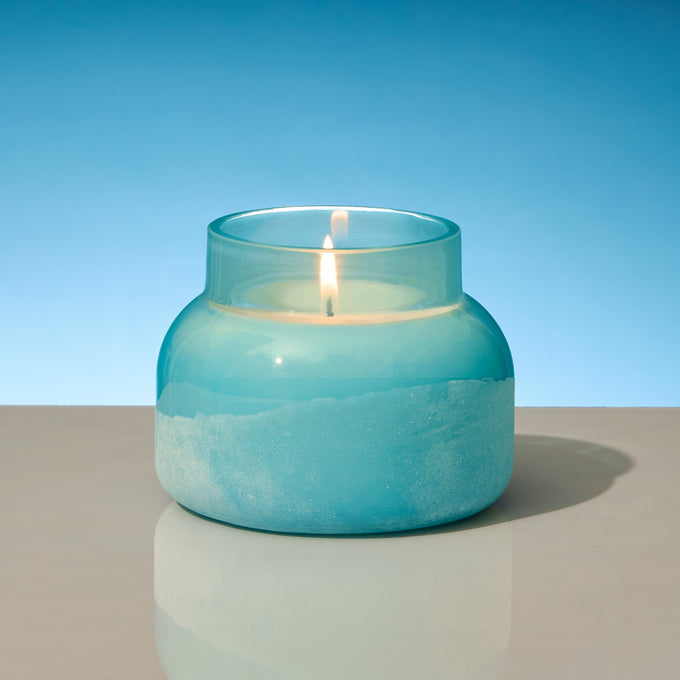 Blue jar candle that is lit on a tan tabletop 