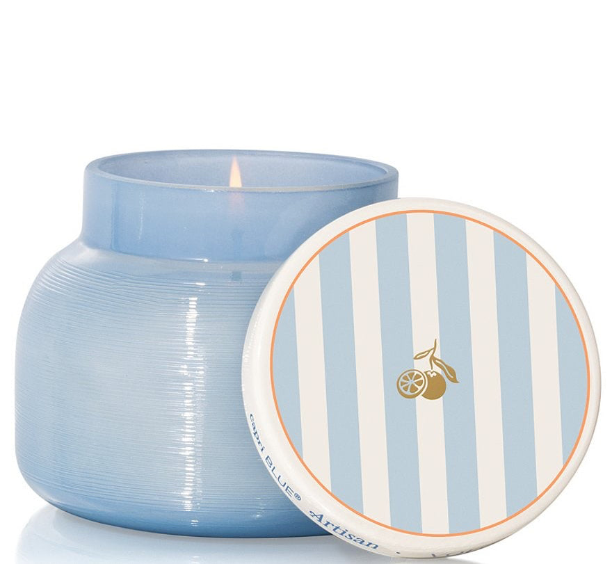 Lit blue candle with a striped lid propped on it - on a white background 