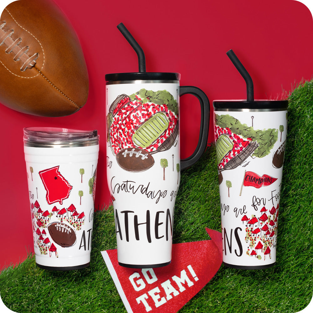Three tumblers with football-themed designs on a grass and red background