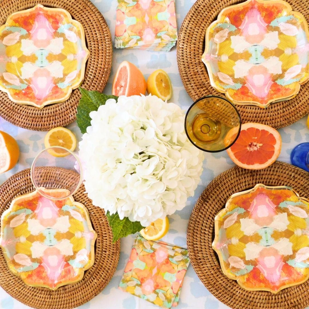 Table setting with Laura Park Marigold floral plates, napkins, and fruit on a white tablecloth.