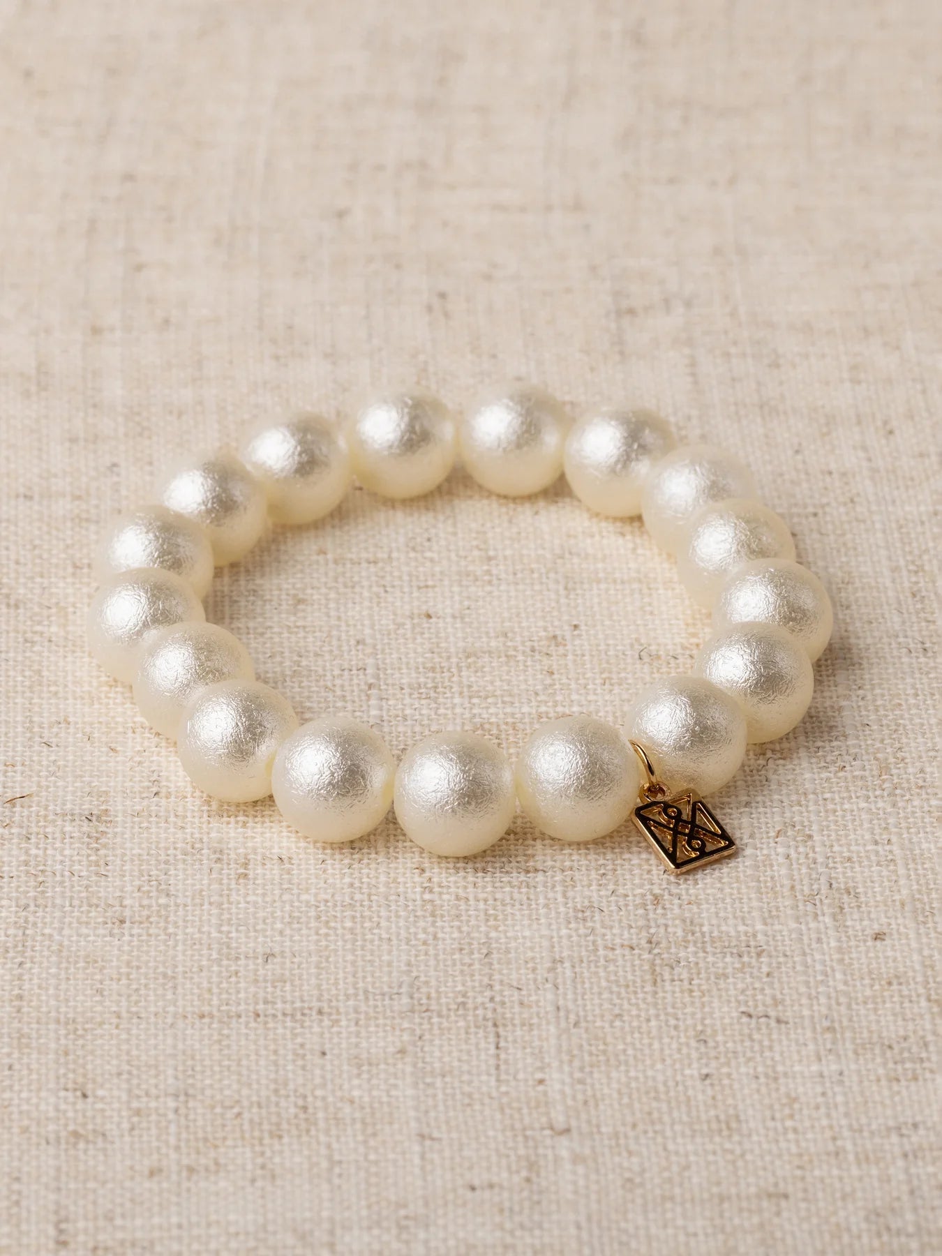 Pearl bracelet with a gold tag on a beige fabric background