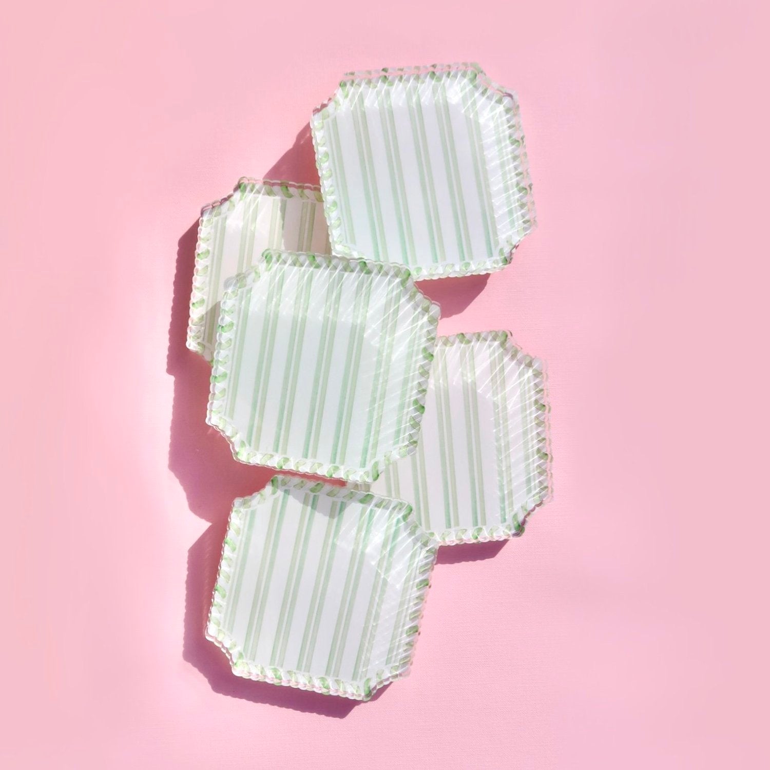 Set of green striped acrylic coasters on a pink background
