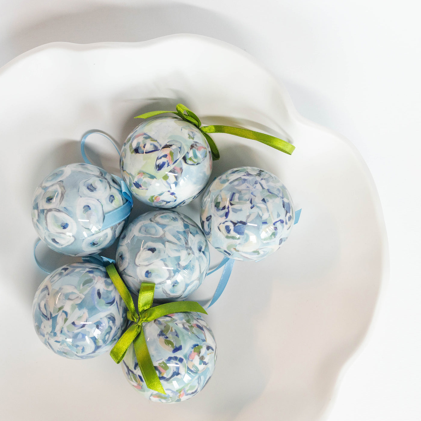 Decorative ornament balls with floral and oyster shell patterns and green ribbons on a white surface