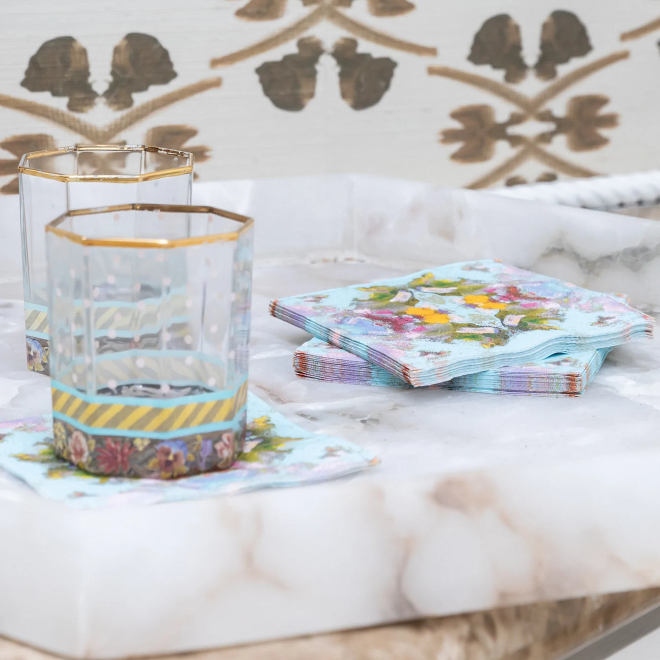 Napkins - Cocktail - Poppy Blue- picture is of a stack of the colorful poppy blue napkins with two cocktail glasses sitting on the napkins ]