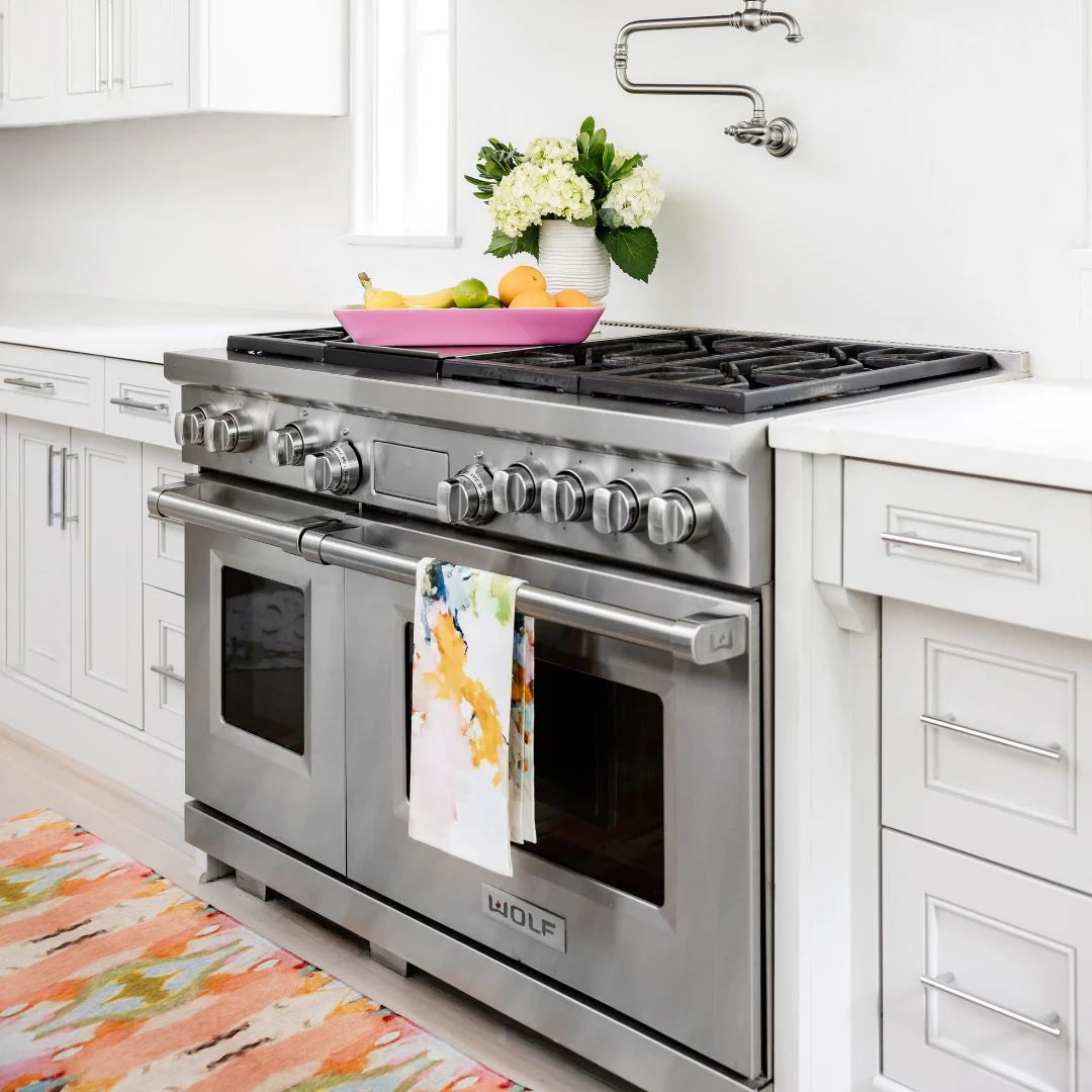 Tea Towel - Under The Sea- this is a picture of the under the sea tea towel design resting on an oven handle, in the picture is also a pink display with fruit in it and a vase of flowers 