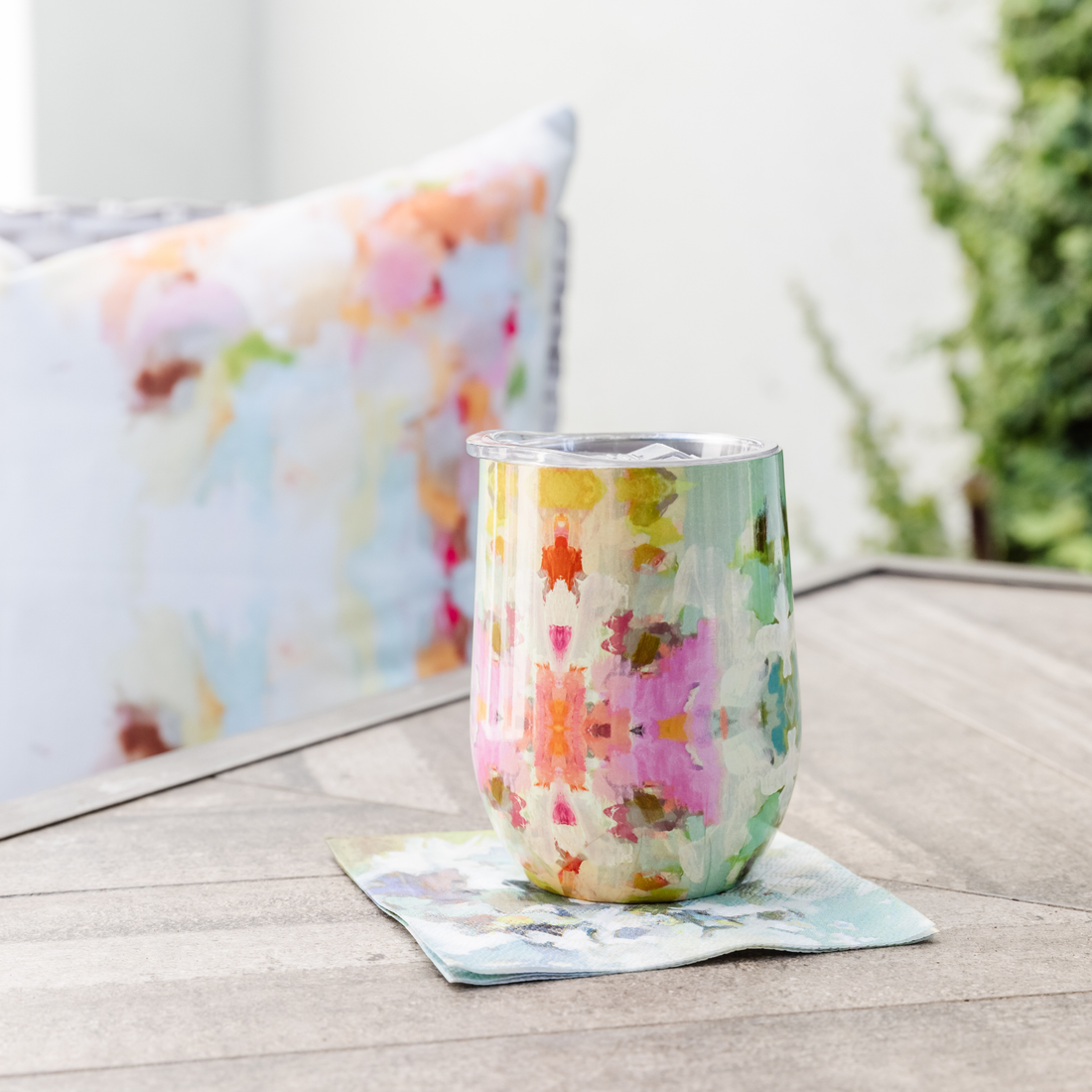 Tumbler - Stemless Wine - Giverny- this is a picture of the giverny design on the wine tumbler with a lid sitting on a napkin on a table with a pillow behind it 